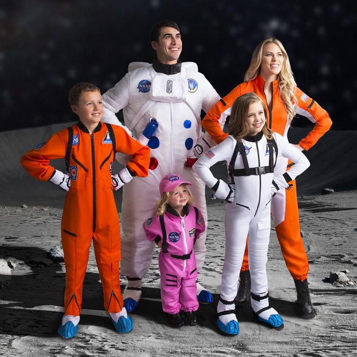 People wear colorful spacesuits while posing confidently on a moon-like surface under a starry sky.