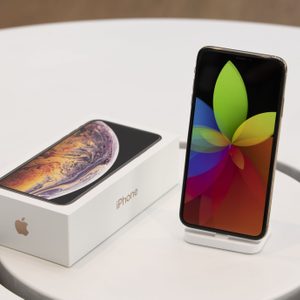 Smartphone displaying colorful flower pattern beside its box, resting on a white circular table in a retail setting.