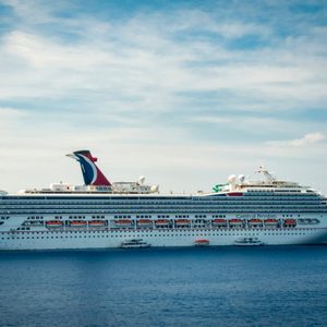 Cruise ship sails on calm ocean under a partly cloudy sky, with 