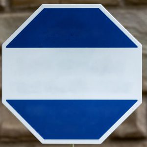 Octagonal sign displays a wide blue band above a stone wall background.