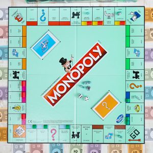 A Monopoly board game lies organized; colorful money, cards, and game pieces surround it, with 
