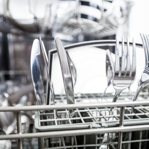 Silverware standing upright in a dishwasher basket, surrounded by racks, ready for washing.