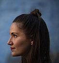 Person stands in profile, observing something, against a blurred blue background.