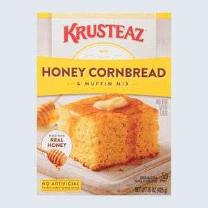 A box of honey cornbread mix displays a cornbread slice topped with butter, illustrating the productâ€™s focal appeal amidst light, inviting packaging.