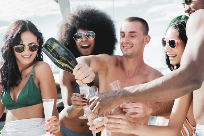 champagne on boat with toothy smiles, happy multicultural friends pouring sparkling wine and smiling.