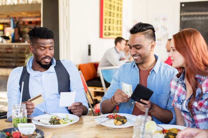 leisure, payment and people concept - happy friends with money and credit card paying bill for food at restaurant