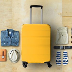 Yellow suitcase centered with travel items including a hat, shoes, camera, and ukulele arranged neatly on wooden floor.