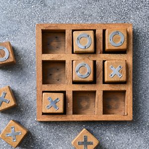 Wooden tic-tac-toe game, X and O blocks, partially placed in grid on textured surface.