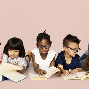 Children read books while lying on the floor against a plain pink background.