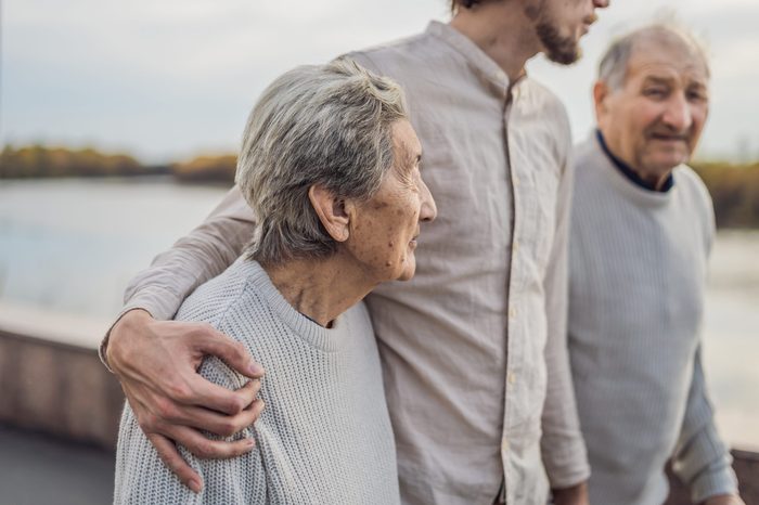 An elderly couple walks in the park with a male assistant or adult grandson. Caring for the elderly, volunteering