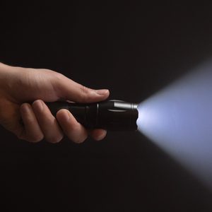 A hand holds a flashlight, emitting a beam of light in a dark background.