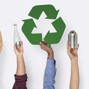 Hands hold recyclable items and a green recycling symbol against a plain background.