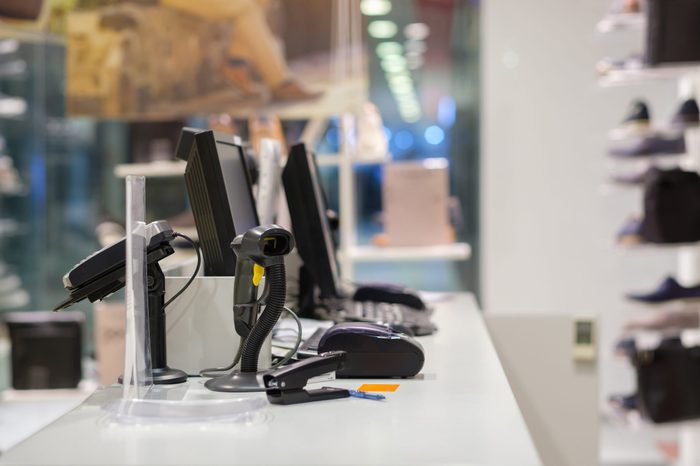 Two cash desks with computer screens and barcode scanners on white table and wall in small store