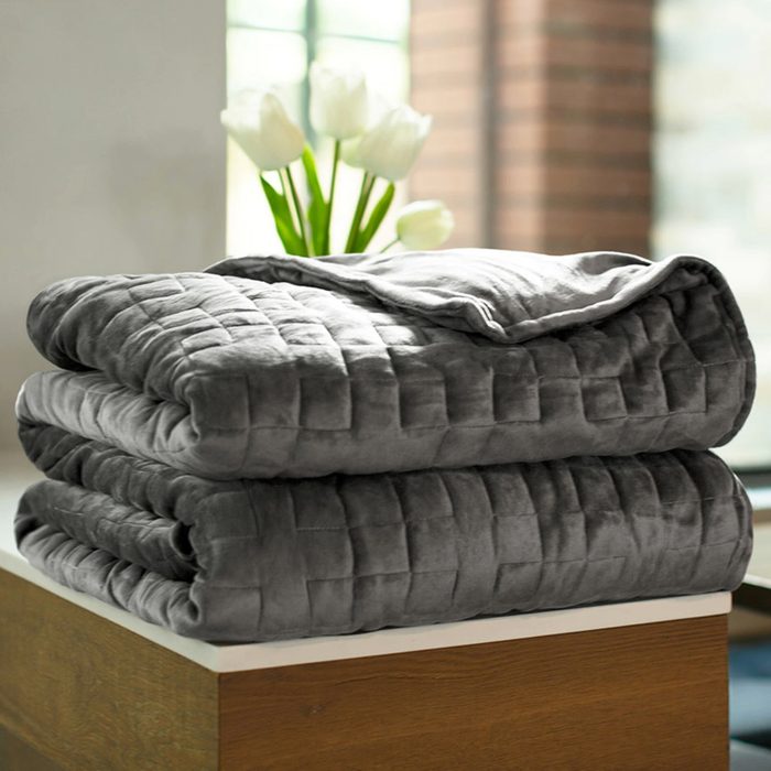 Folded gray quilt rests on a wooden surface, with white tulips and blurred windows in the background.