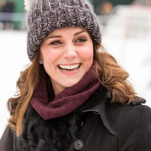 Woman smiling, wearing a knit hat and scarf, outdoors, with blurred snowy background.