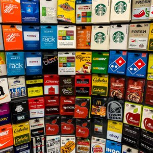 Gift cards hang on a display rack, featuring various brands like Amazon, GameStop, and Starbucks, offering diverse purchasing options in a store setting.