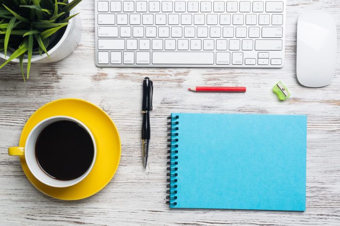 Top view conference table with office accessories. Break time at workplace. Flat lay wooden desk with computer keyboard and mouse, cup of coffee, spiral notebook and green plant in pot.