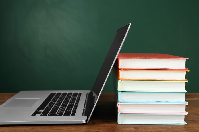 Stack of books with laptop on table in classroom