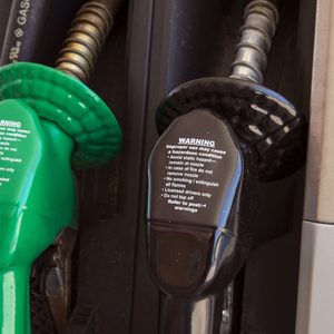 Gas pump nozzles hang; one green, one black; displaying safety warnings in a fueling station context.