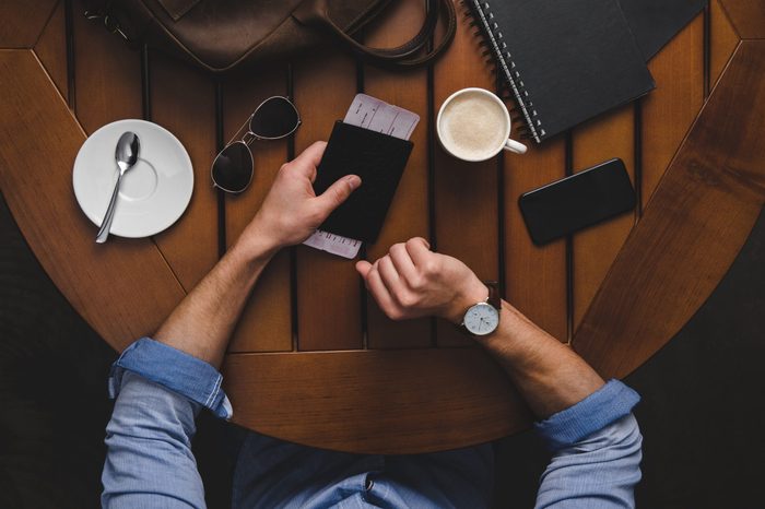 overhead view of man with passport and air ticket sitting at wooden table with coffee and leather bag