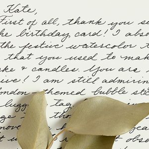 Handwritten letter expressing gratitude for a birthday card, mentioning watercolor techniques, accompanied by dried leaves on paper.