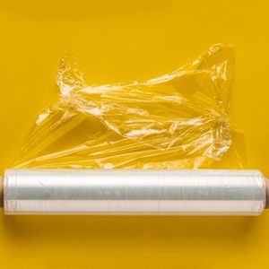 Plastic wrap roll partially unravels, resting on a bright yellow background.