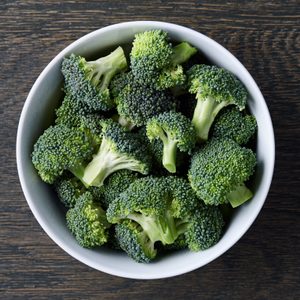 Broccoli pieces rest in a white bowl atop a dark wood table, creating a vibrant contrast.