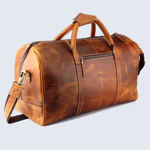 Leather duffel bag rests on a light background, displaying a rich brown color with stitched handles and an attached shoulder strap.