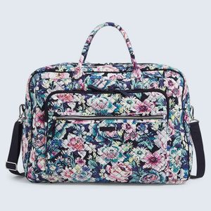 Quilted bag displaying vibrant floral design, resting on a plain background; features multiple pockets, handles, and a detachable black strap for carrying.