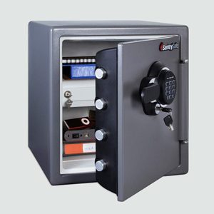 A gray safe stands open, displaying shelves containing a notebook, a blue box, keys, electronic devices, and documents, set against a plain background.