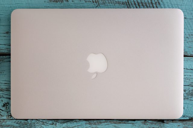 Closed silver laptop resting on a weathered blue wooden surface, displaying a partially bitten apple logo in the center.