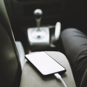 A smartphone charges on a car's armrest with gear shift visible, surrounded by vehicle's interior seats.
