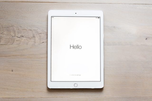 Tablet displays "Hello" on a white screen, placed on a light wooden surface.
