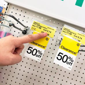 Finger pointing at a clearance tag; price reduced from $11.49 to $5.74 for Cricut Vinyl Shimmer Purple. Shelving has a 50% off sign.