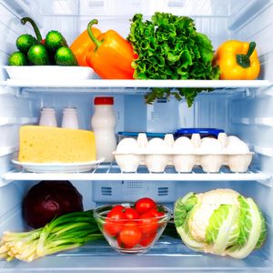 Vegetables and dairy are organized in a refrigerator, including bell peppers, lettuce, cucumbers, cheese, milk, eggs, tomatoes, cauliflower, and green onions.