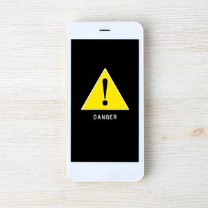 Smartphone displays yellow warning triangle with exclamation mark, labeled 