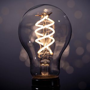 A lit spiral filament bulb glows warmly against a softly blurred, dark background, creating a cozy and focused atmosphere.