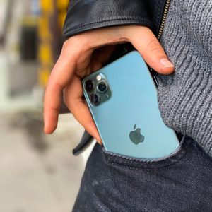 Hand holding a sleek smartphone with multiple cameras, near a denim pocket, with a blurred urban background.