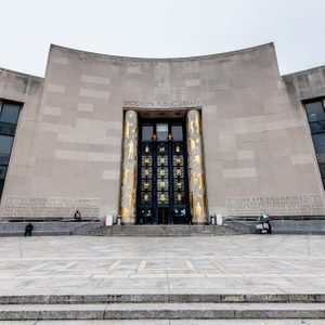 Library entrance adorned with golden artwork, standing prominently; surrounding steps lead to the door, flanked by inscribed gray walls on a cloudy day.