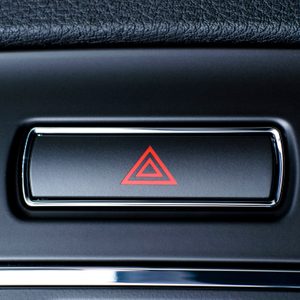 A black rectangular button displays a red triangle symbol, situated on a textured dashboard surface, likely within a vehicle interior.