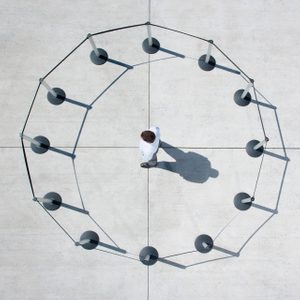 A person walks inside a circular barrier of stanchions and ropes on a concrete surface.