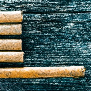 Five cigars lie on a textured, dark wooden surface, four aligned above and one placed separately below.