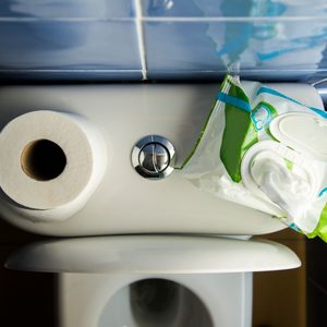 Toilet tank holds a roll of toilet paper and an opened pack of wipes in a tiled bathroom environment.