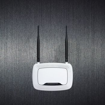A white router with two antennas sits against a textured gray wall, centered and inactive.