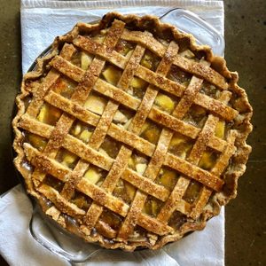 Pie with a lattice crust sits on a towel, resting on a dark, textured surface.