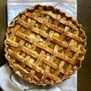 Pie with a lattice crust sits on a towel, resting on a dark, textured surface.
