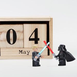 Lego figures duel with lightsabers before a wooden calendar displaying 
