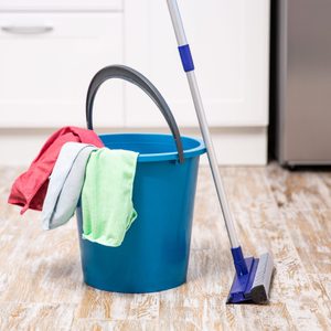 A blue bucket holds cleaning cloths, standing next to a mop on a wooden kitchen floor.