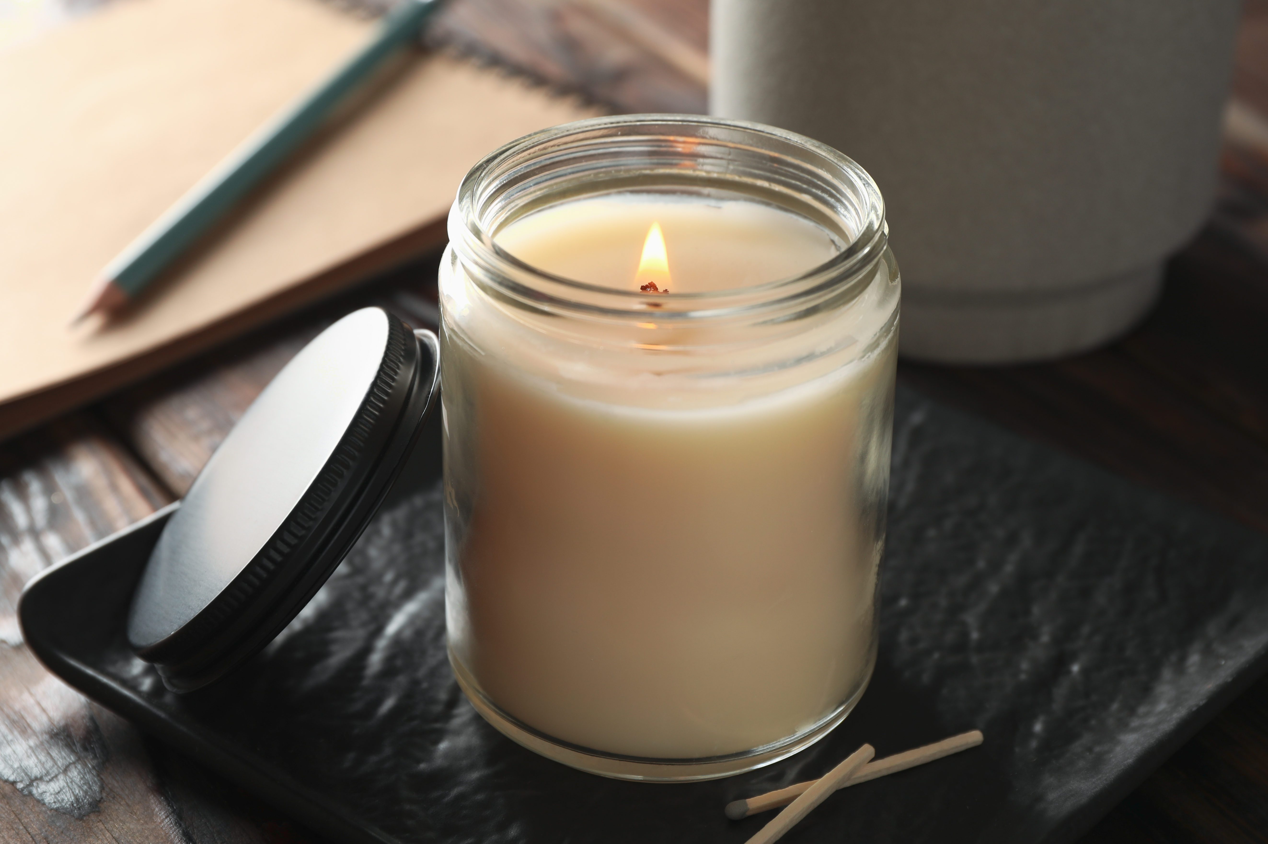 Burning candle in glass jar, succulent and notebook on wooden background, close up