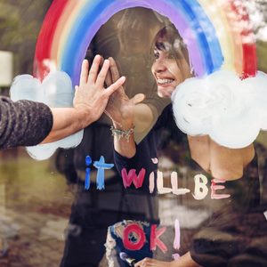 Hands touch glass, one inside with a woman smiling, a rainbow painted with 